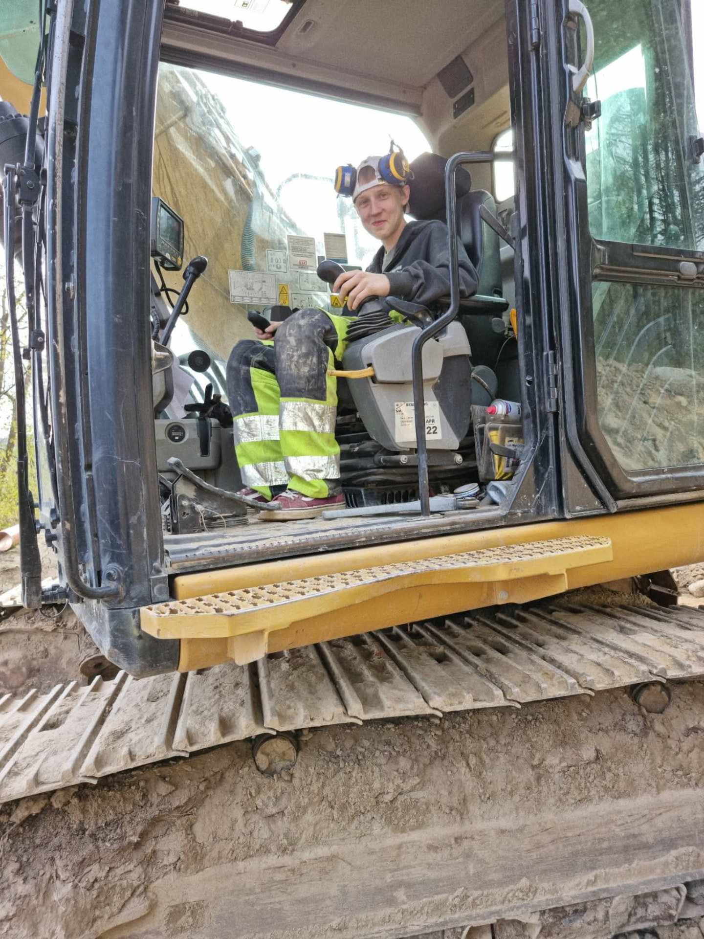 Nathan sitter i förarhytten på en grävmaskin i arbetskläder