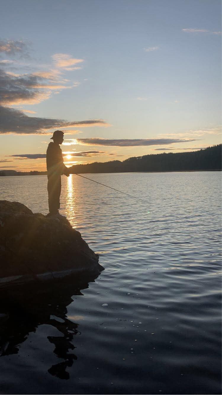 Nathan fiskar från en klippa i solnedgången